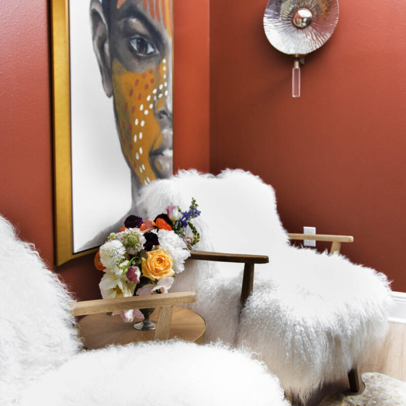 photo of sitting area with two club chairs covered in faux fur, painted coffee table and two large graphic art pieces in the background | bold red sitting room