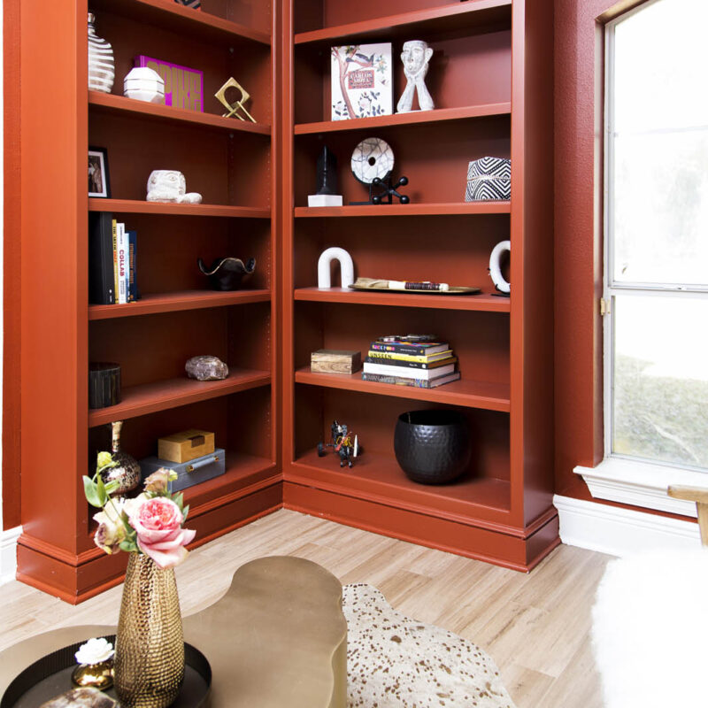 photo of two corner bookcases, painted in red-orange color, adorned with accessories | bold red sitting room