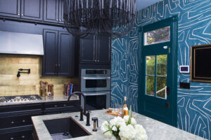 Bold blue kitchen designed by Whitney J Decor with warm wood shelving, brass accents, and curated decorative styling.