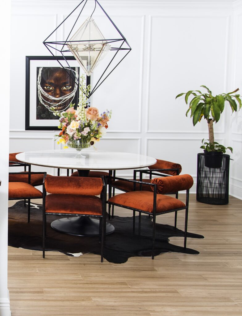 Modern dining room with terracotta velvet chairs, a round white table, geometric pendant light, floral centerpiece, and a large portrait artwork on a paneled white wall. Caption A warm, modern dining room layered with terracotta tones, sculptural seating, and expressive artwork. Description This modern dining room blends warm terracotta seating with a crisp white round table, geometric pendant lighting, and a striking portrait that anchors the space. Styled with a floral centerpiece, cowhide rug, and a tall potted plant, the room balances contemporary lines with expressive, art‑driven character. Designed by Whitney J Decor in New Orleans. Suggested File Name (if you ever upload a new version) terracotta-dining-room-new-orleans-whitney-j-decor.jpg Why this metadata works - Alt text is descriptive and keyword‑rich without stuffing. - Title aligns with your editorial naming system. - Caption adds context for users and search engines. - Description gives Google a full understanding of the room, location, and design style. - File name is optional to change, but this version is SEO‑ideal for future uploads. If you want, I can generate metadata for every image in this project so your entire portfolio stays consistent and optimized.